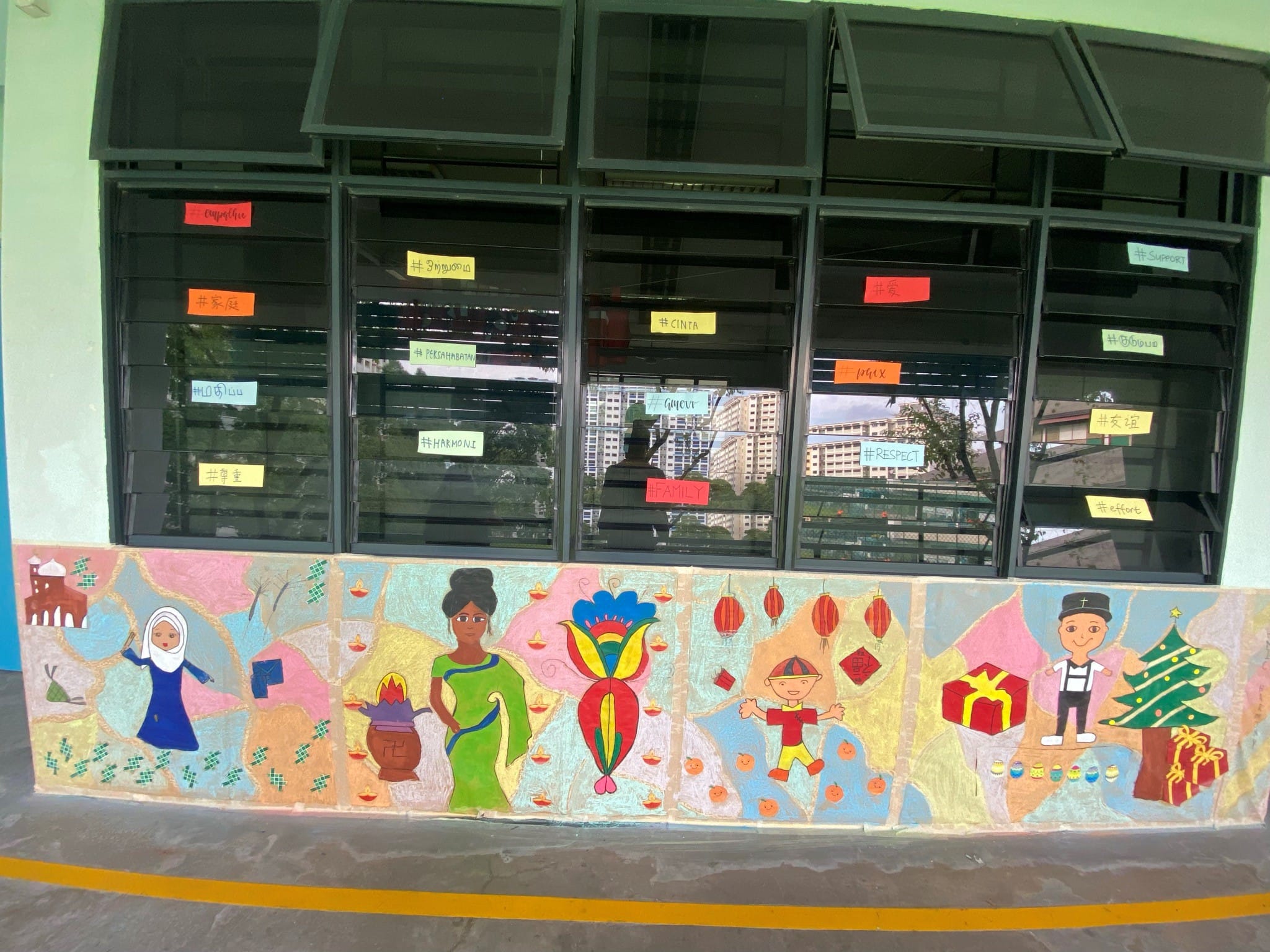 Colorful mural below windows showing multicultural figures celebrating Eid, Diwali, Chinese New Year, and Christmas.